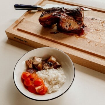 pork belly adobo on a butcher block and a bowl of pork belly adobo served with cherry tomatoes and jasmine rice