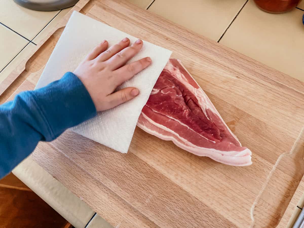 child patting pork belly with a napkin