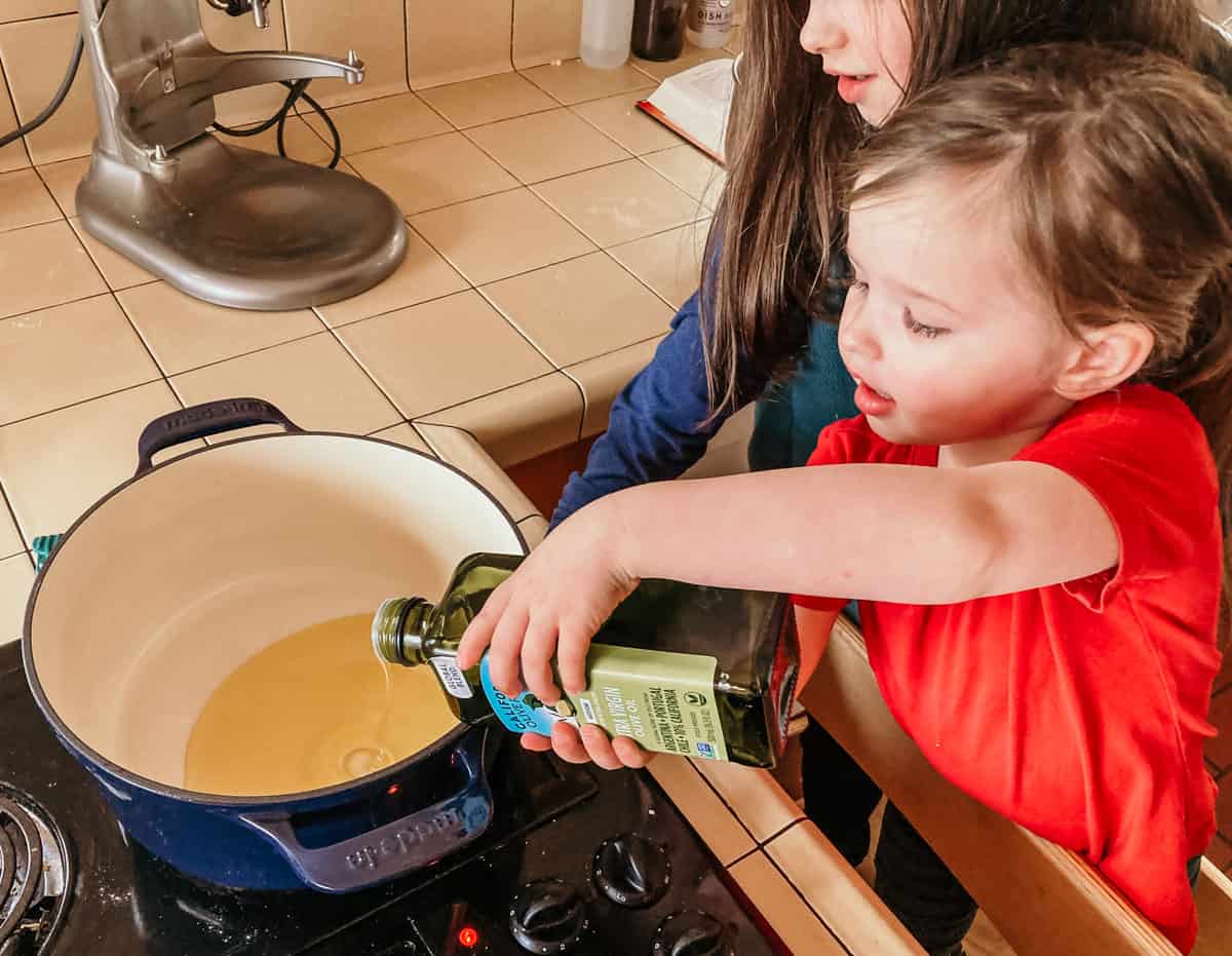 child pouring olive oil into a dutch oven