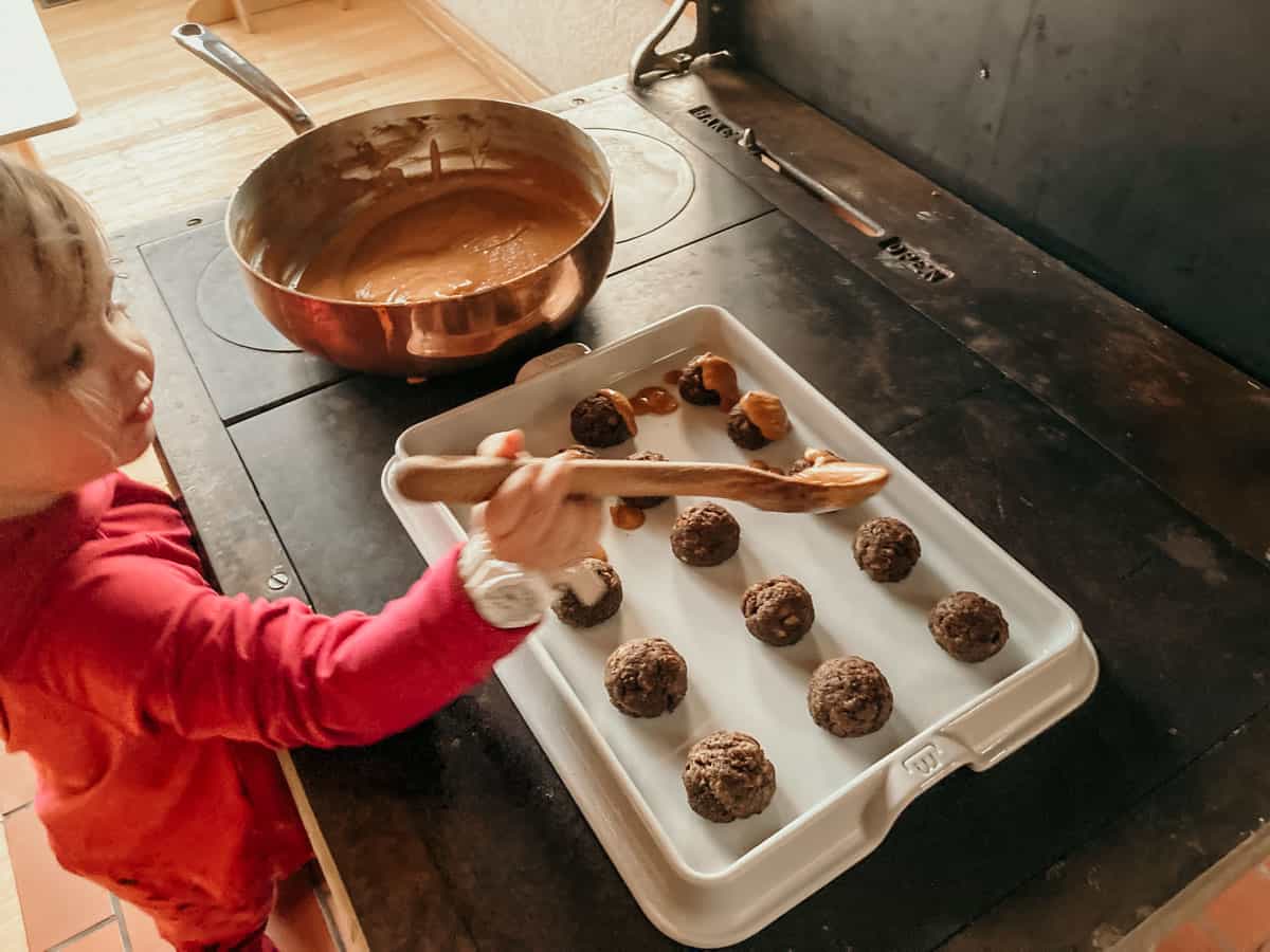 child spooning The Mother Africa Sauce onto bison meatballs on a Made In baking slab using a wooden spoon