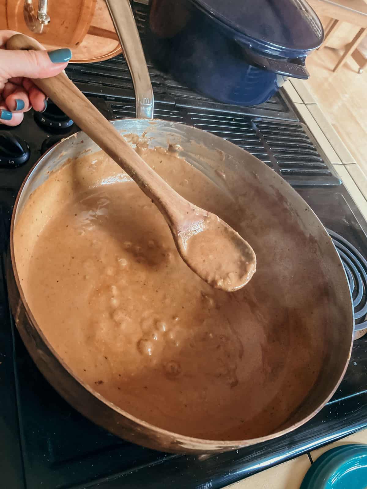 closeup of West African Peanut Sauce in a saucier and on a wooden spoon