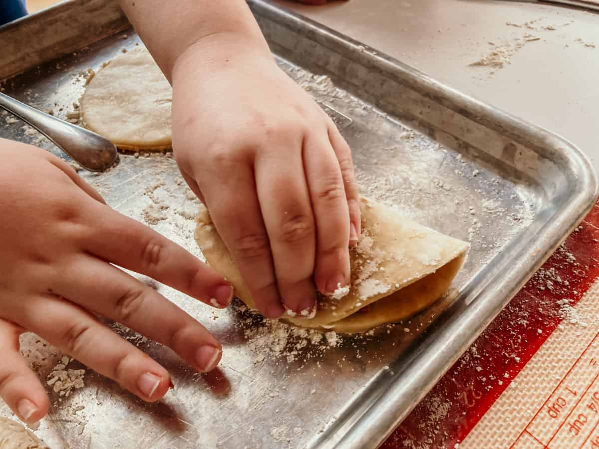 child pressing down the corners of folded empanadilla dough