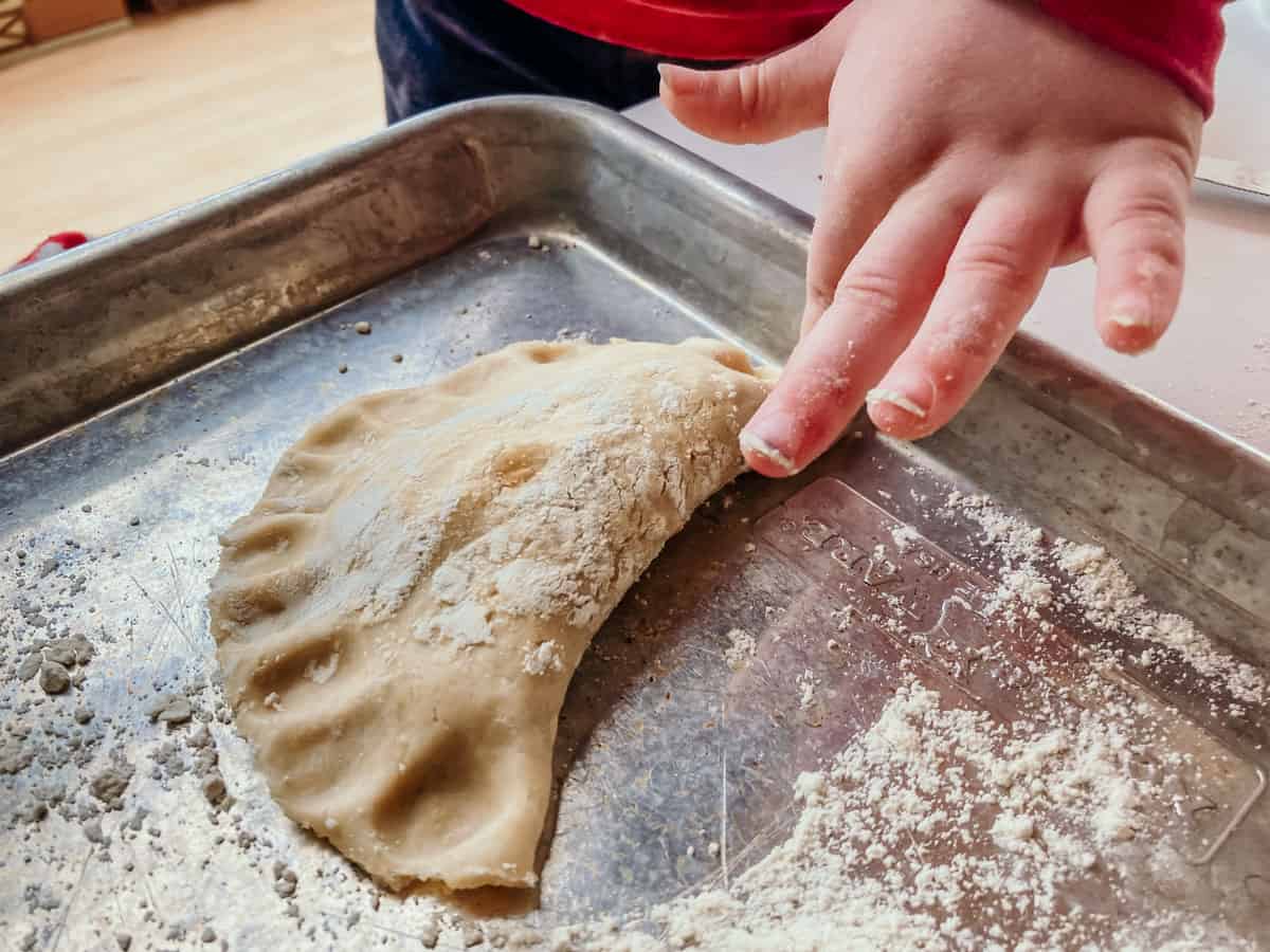 child pressing their finger into the edge of an uncooked empanadilla