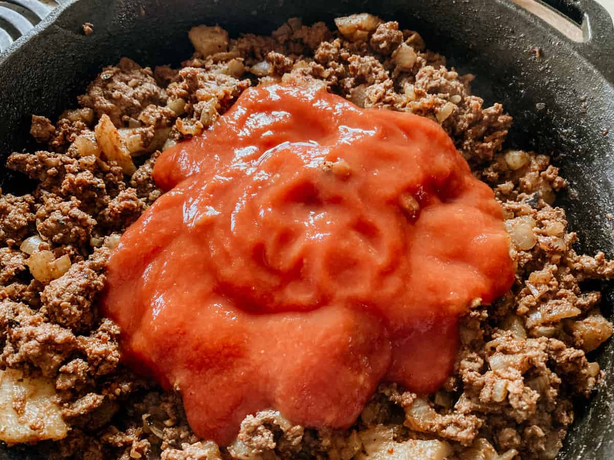 tomato sauce in a cast iron skillet with picadillo ingredients