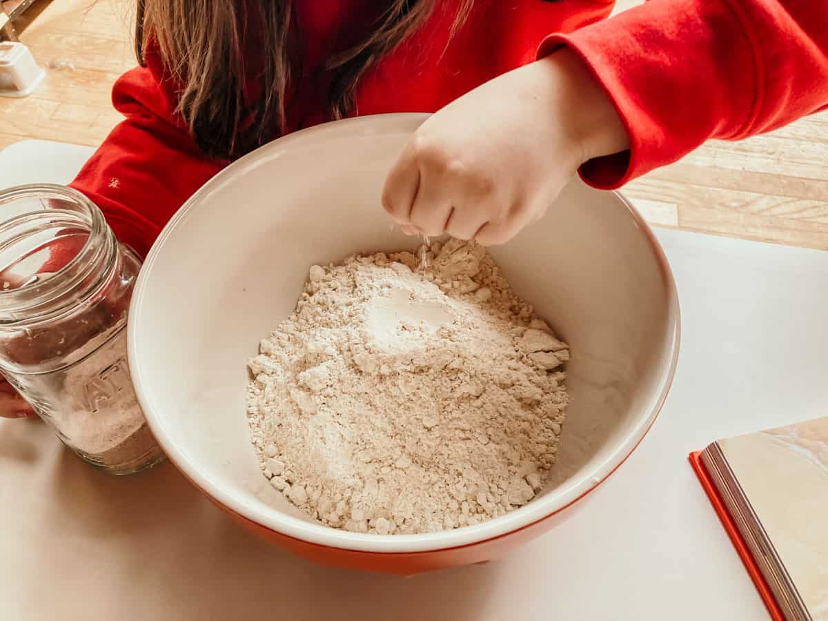 child adding a pinch of salt to a bowl of all-purpose einkorn flour