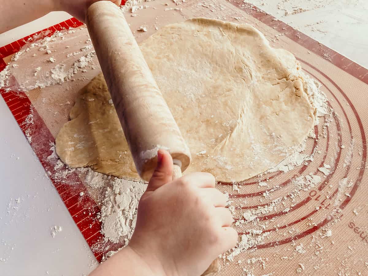 closeup of a child rolling out empanadilla dough over a silicone baking mat
