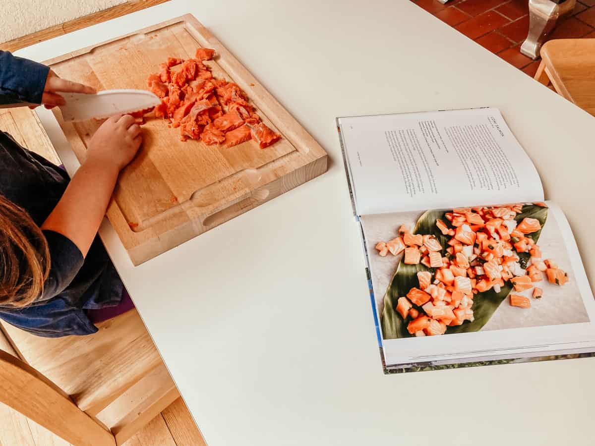 child slicing salmon filet next to Cook Real Hawai'i cookbook