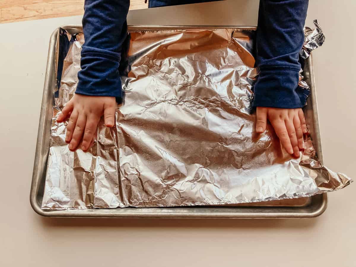 child's hands lining a sheet pan with aluminum foil