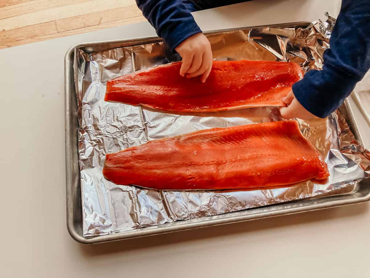 child placing salmon fillets on a sheet pan