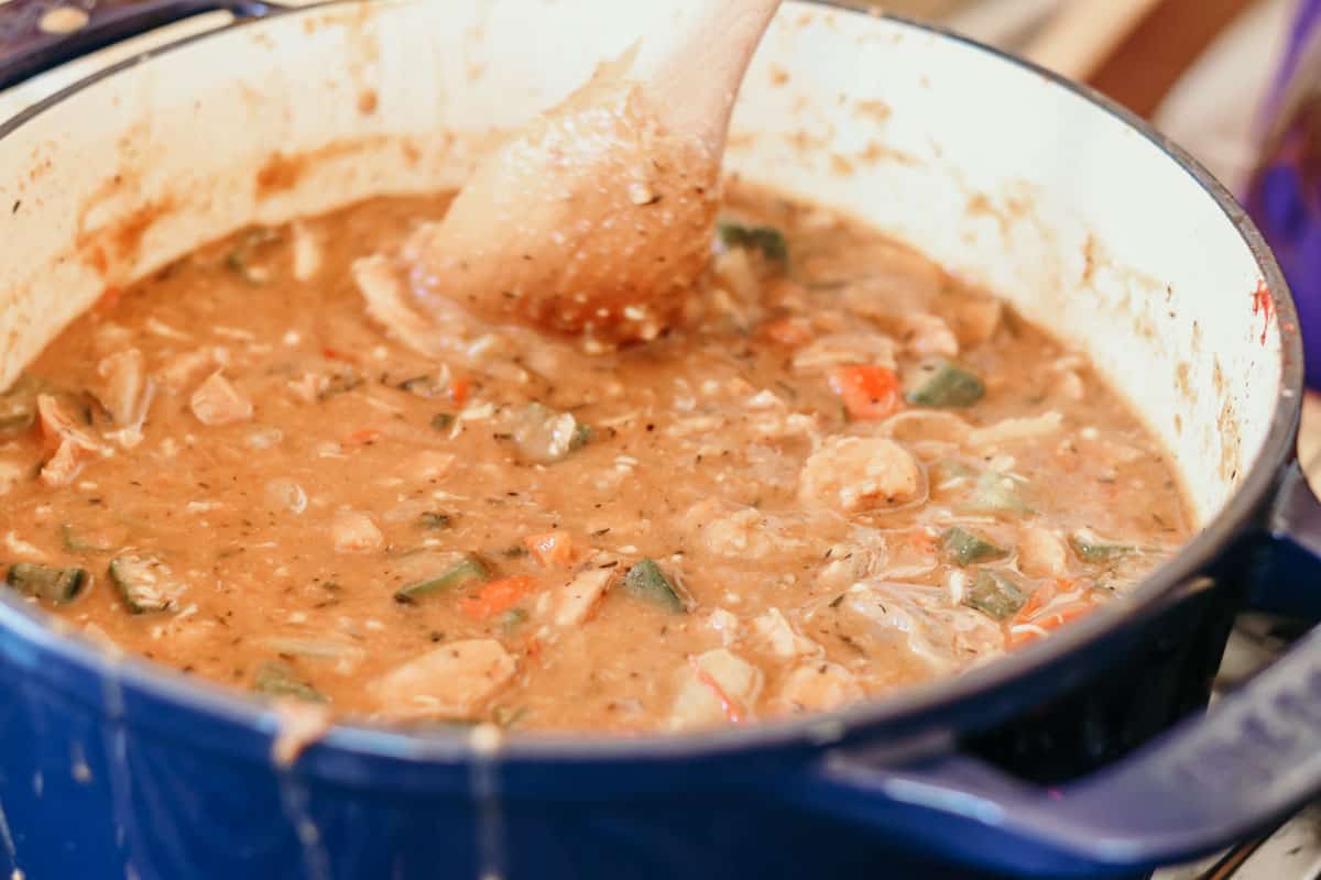 closeup of a wooden spoon stirring Afro-Asian-American Gumbo in a Dutch oven