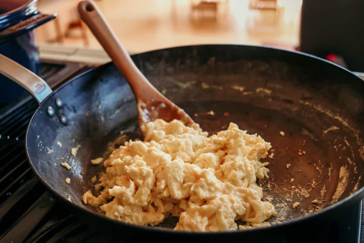 Scrambled eggs in a 12" Made In blue carbon steel pan with a wooden spoon