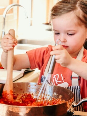 a child stirring piri piri sauce using a wooden spoon and a whisk