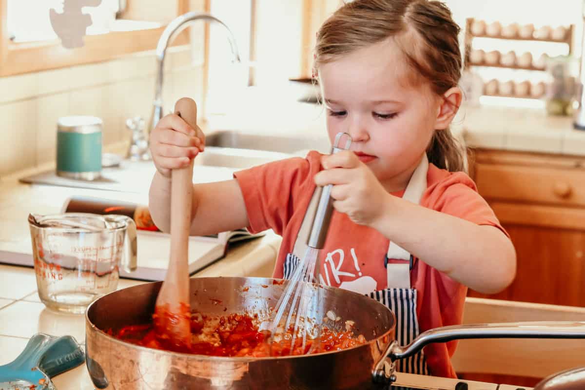 a child stirring and whisking piri piri sauce in a copper saucier