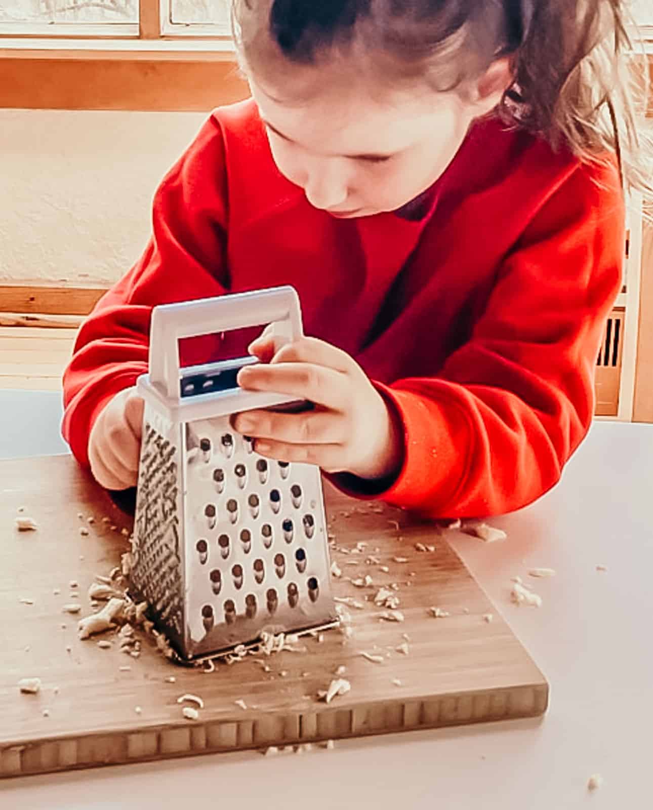 child grating cheese using a box grater and a cutting board