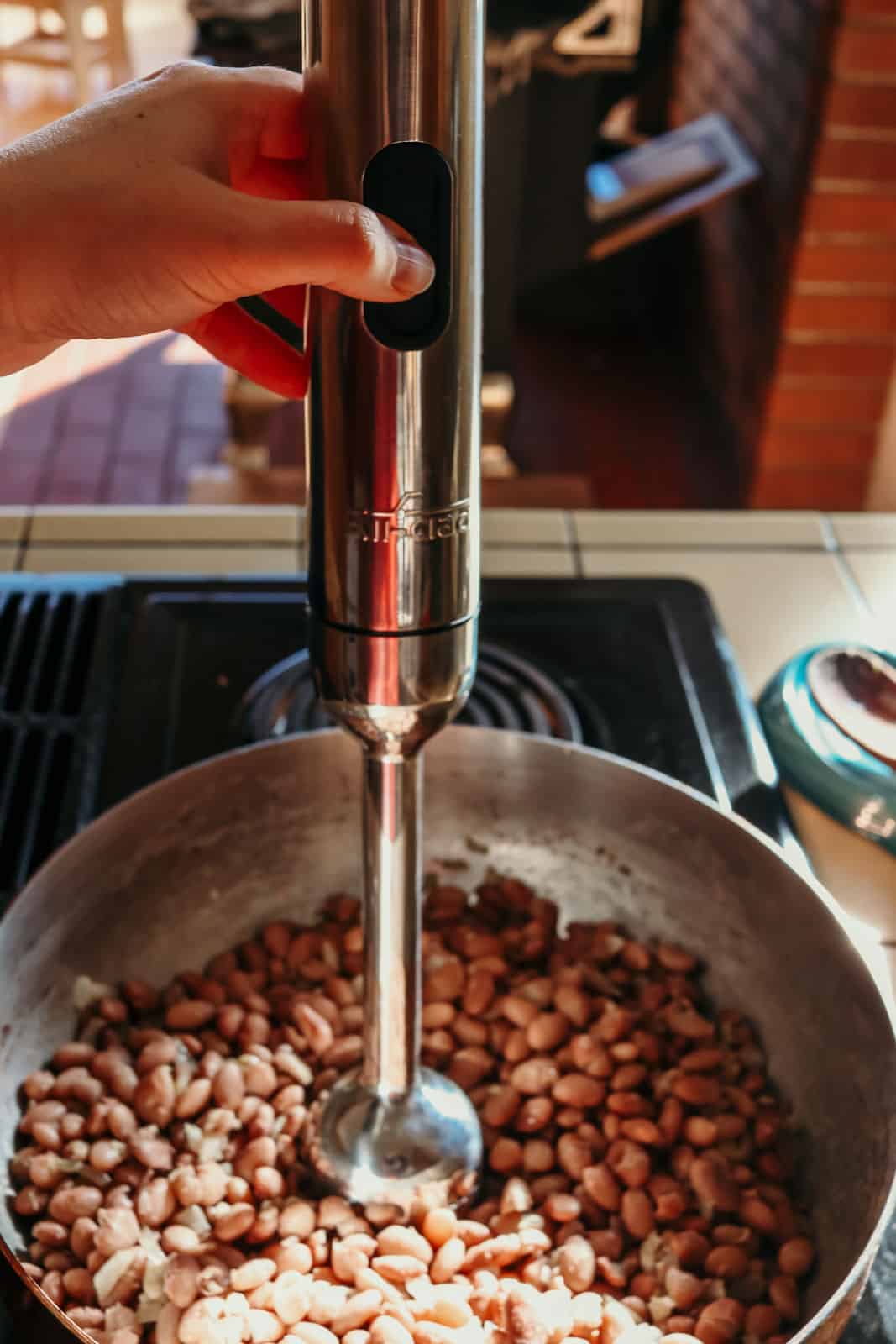 An immersion blender being used to make refried beans in a copper saucier