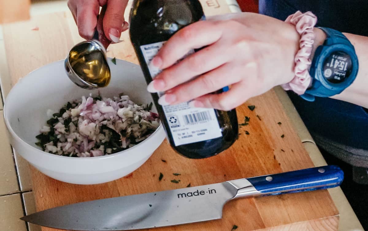 adding extra-virgin olive oil to a mise en place bowl with salsa verde ingredients
