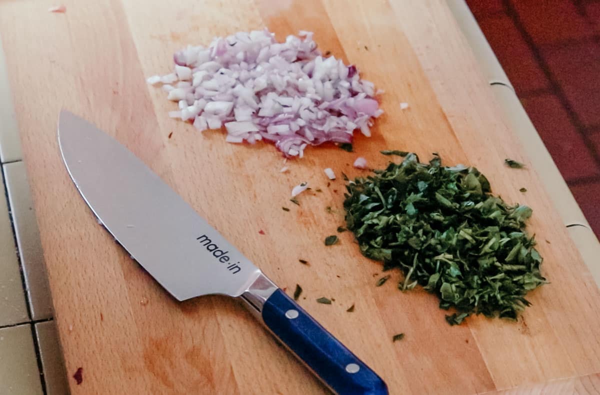 chopped parsley and shallot on a butcher block beside a chef knife