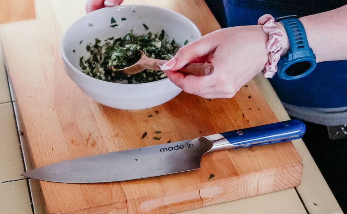 salsa verde on a wooden spoon and in a mise en place bowl on a butcher block
