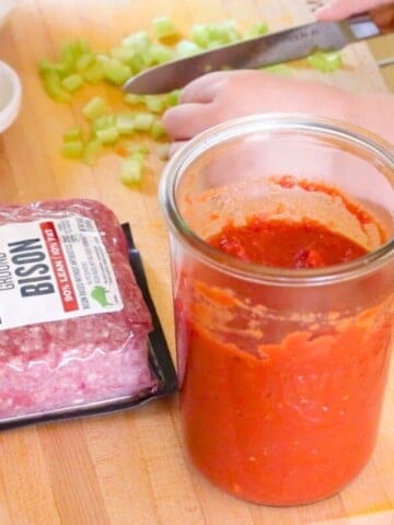 ground bison meat and homemade tomato sauce on a butcher block beside Noah chopping celery