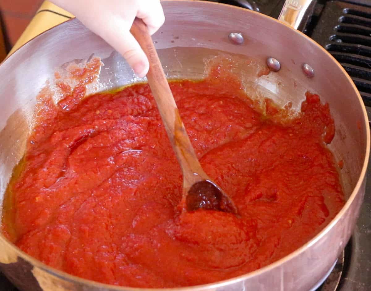 Noah is stirring the tomato sauce with a wooden spoon