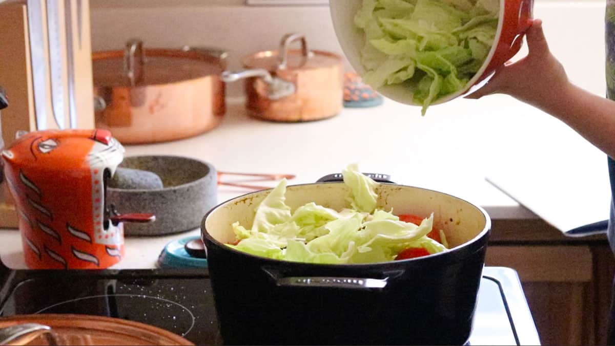 adding cabbage on top of bigos ingredients