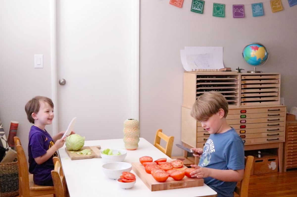John is chopping cabbage on a cutting board and Steve is slicing tomatoes in half