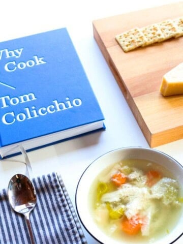 Why I Cook, chicken soup in a bowl, on a butcher block: saltines, parmesan cheese, a cheese knife, and a box grater