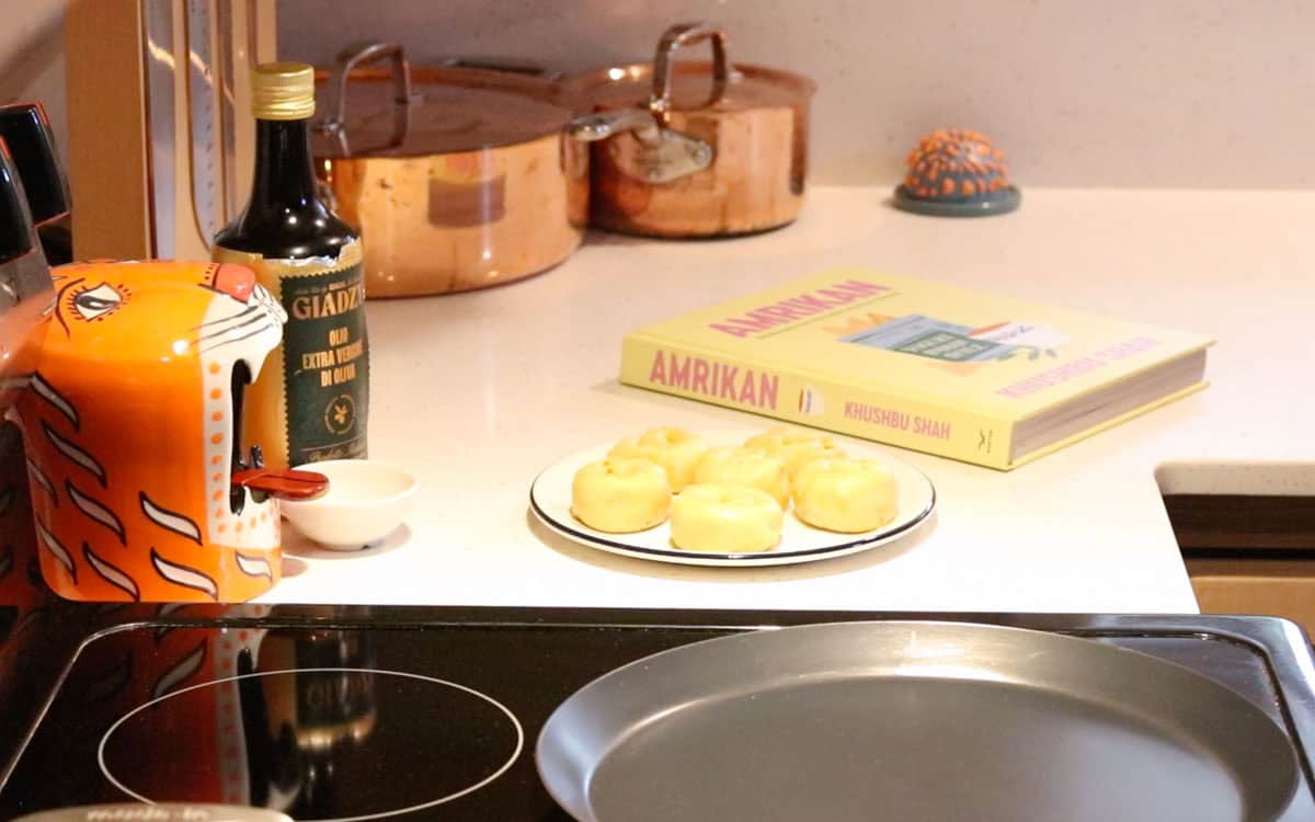 rolled up parathas dough on a plate beside Amrikan cookbook, a tawa, and Giadzy extra virgin olive oil