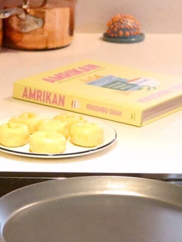 rolled up parathas dough on a plate beside Amrikan cookbook and a tawa