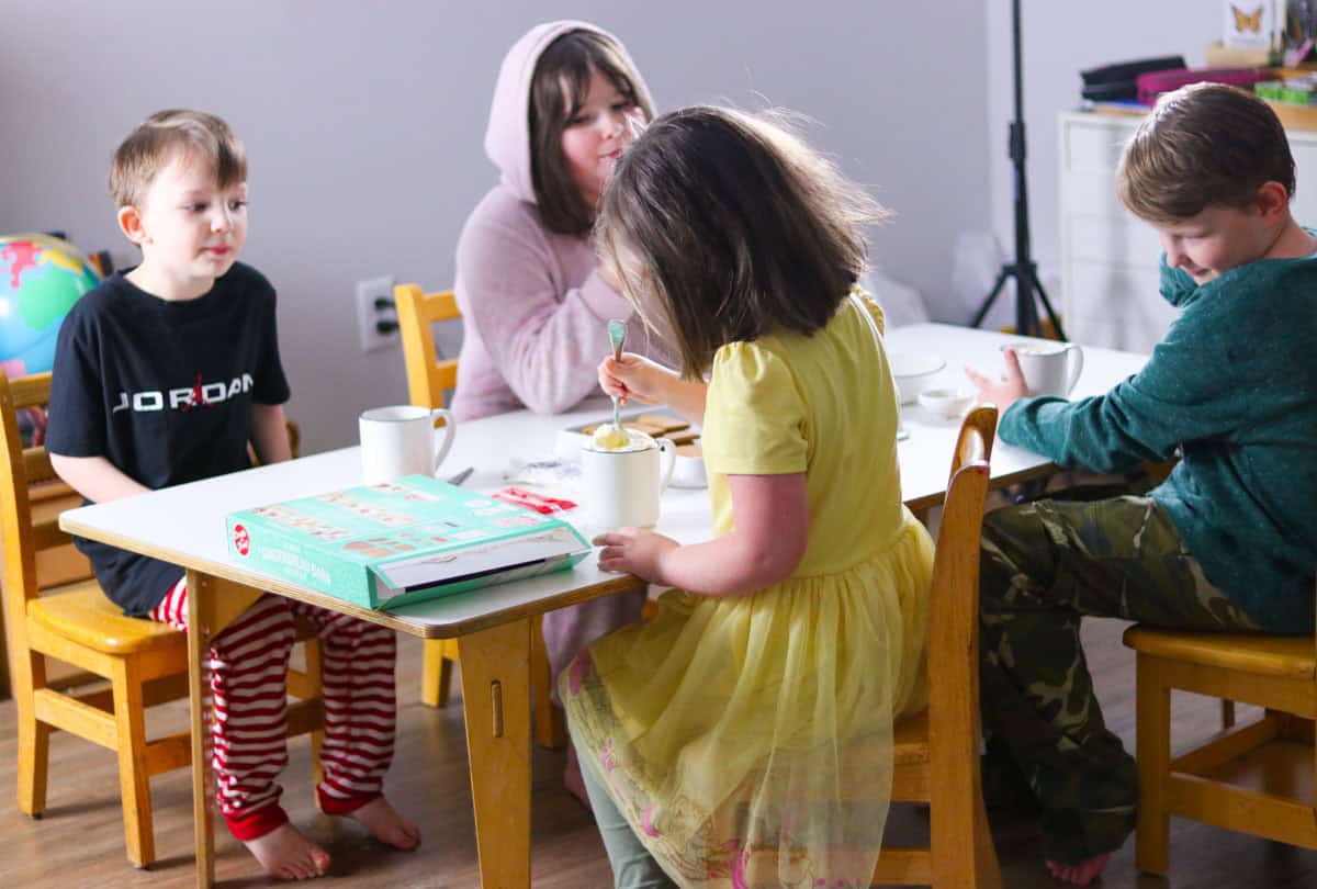 Katalina is stirring her whipped cream into her eggnog while everyone watches and wonders when she's going to be ready to build a gingerbread barn