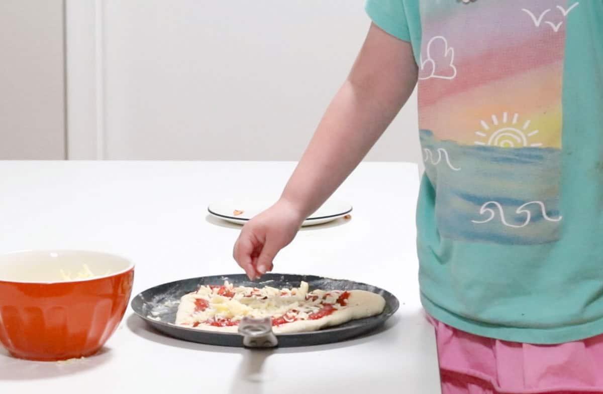 Katalina is adding mozzarella cheese to her pizza