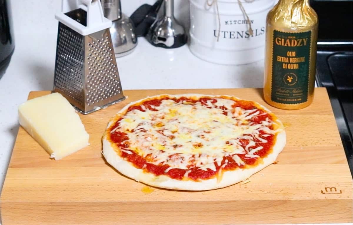 pizza on a butcher block with Giadzy olive oil and a box grater