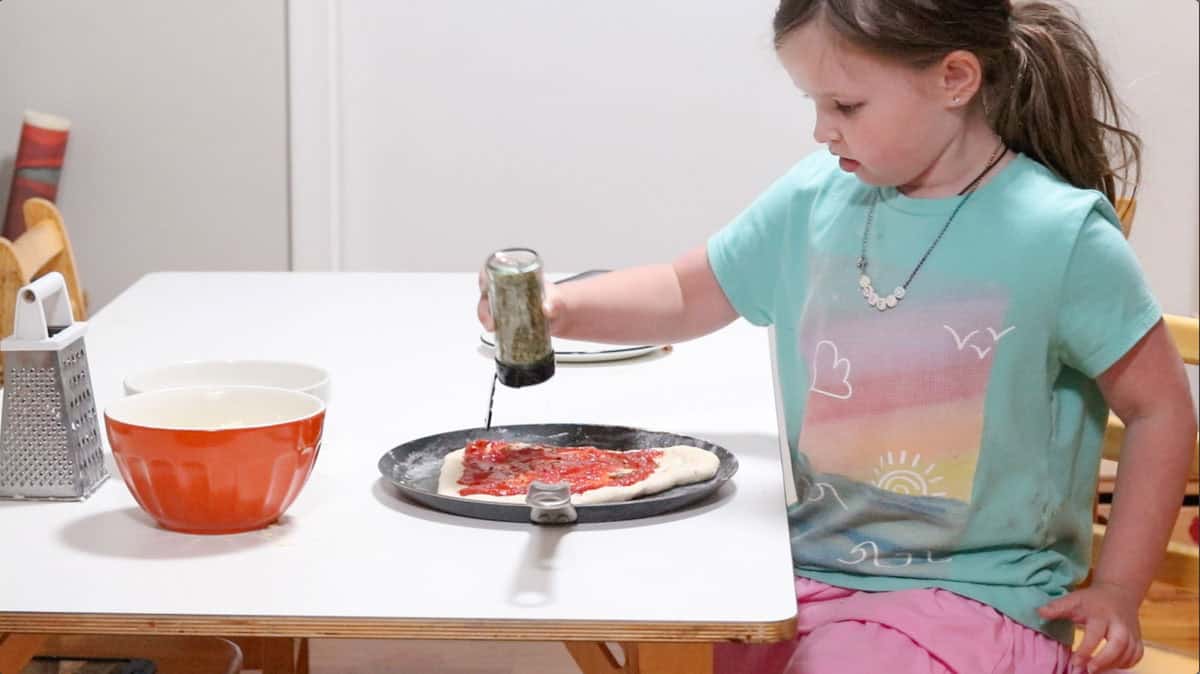 Katalina is adding oregano to her pizza