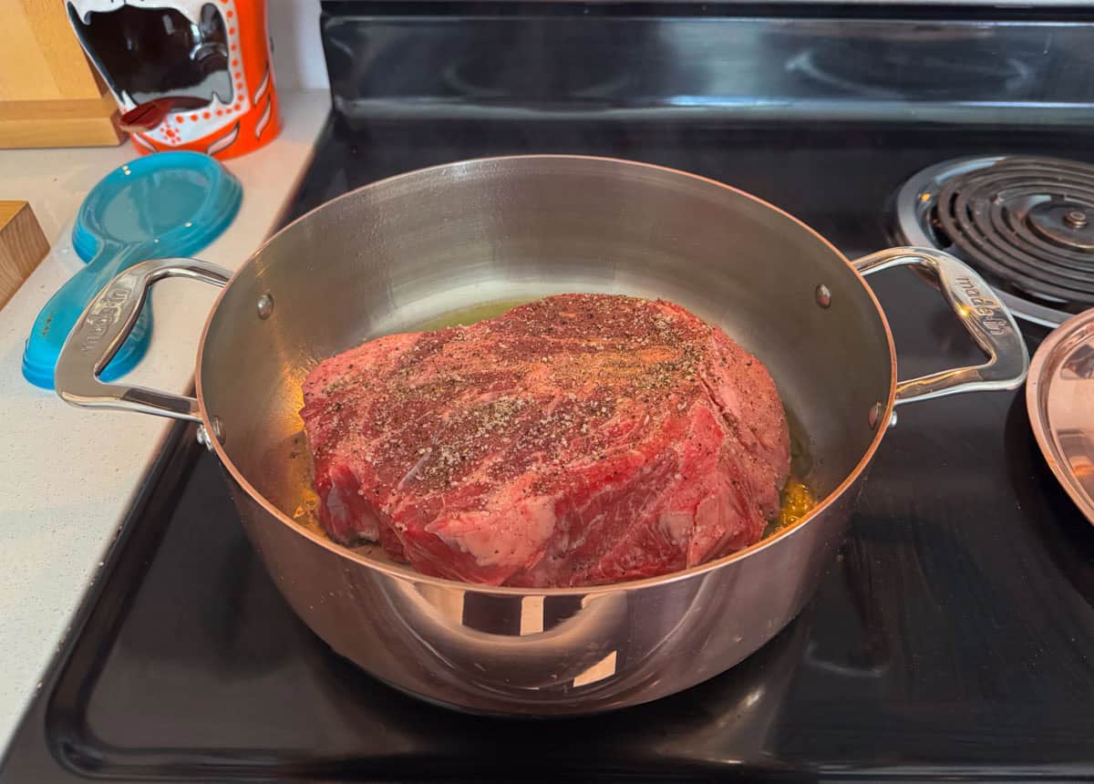 seasoned beef chuck roast braising in a copper rondeau