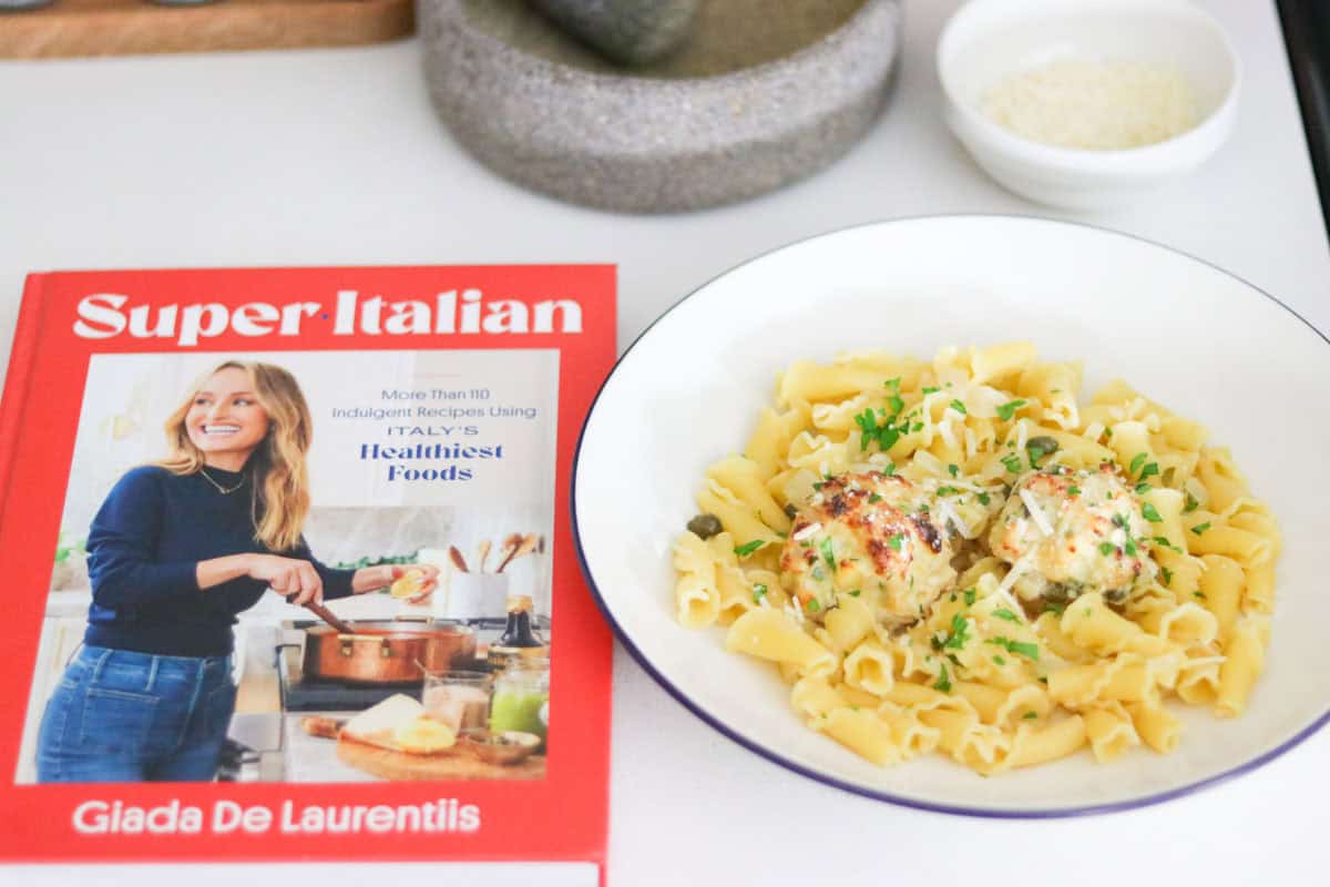 Super-Italian cookbook and chicken piccata meatballs over campanelle, topped with parsley and parmigiano-reggiano cheese