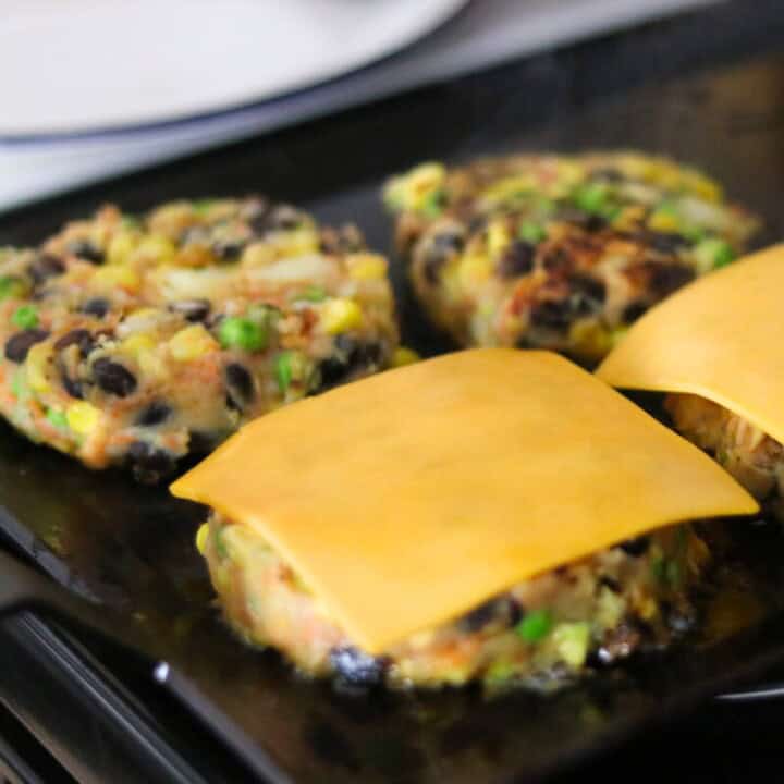 masala veggie burgers, some with cheese, cooking on a griddle