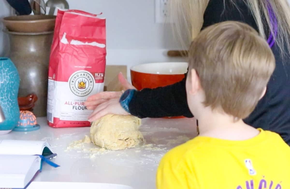 Kristin is folding dough on a countertop and Noah is taking a break