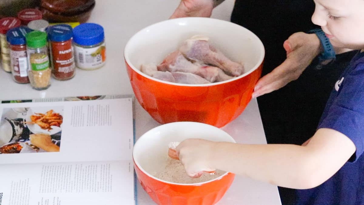 John is using a measuring spoon to add seasoning to raw chicken wings
