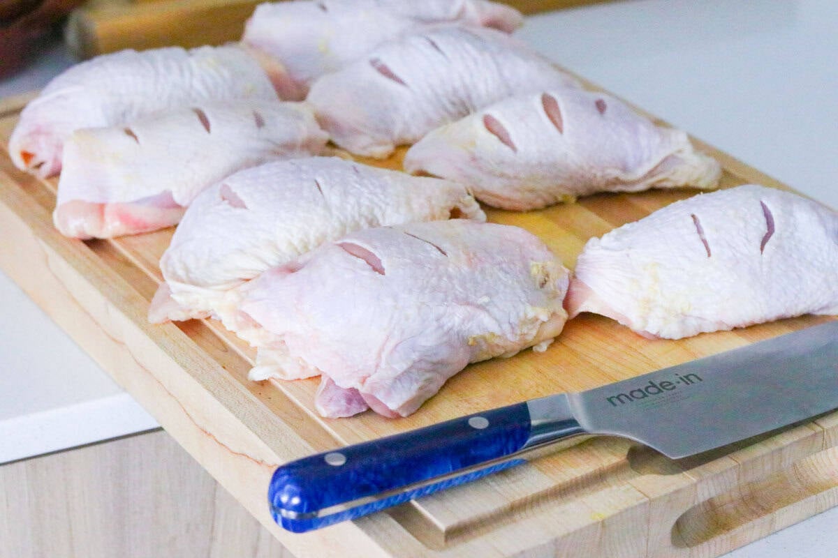raw chicken thighs on a butcher block next to a chef knife