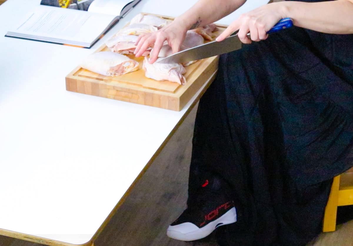 Kristin is cutting into the chicken thighs using a knife and cutting board