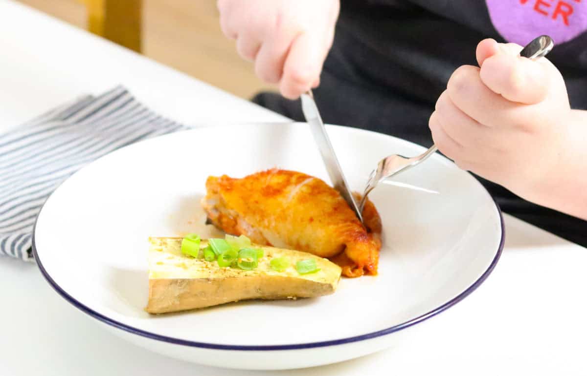 Kaia is cutting into gochujang chicken with a fork and knife