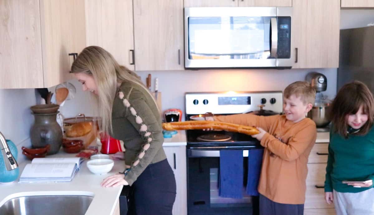 Noah is poking Kristin in the back with a baguette