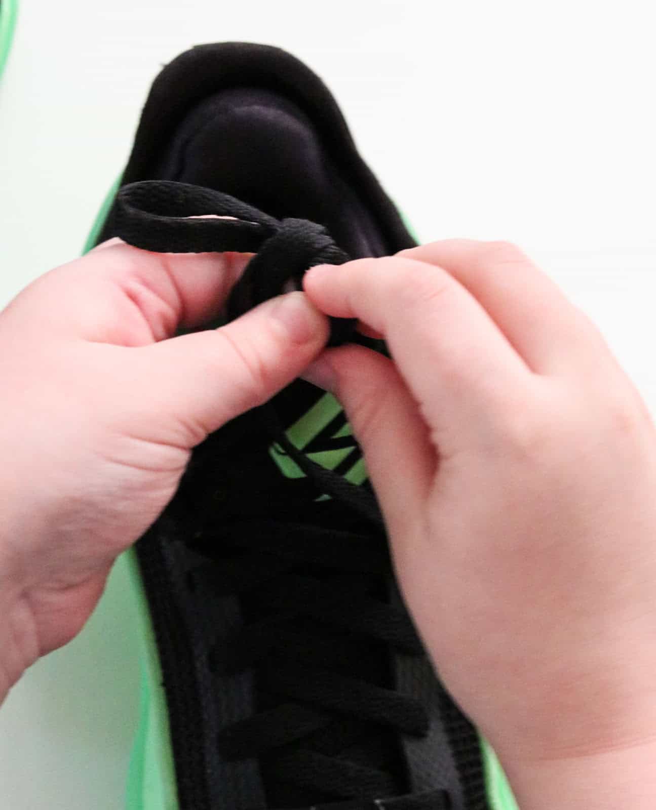 Noah is pulling the bunny ear of his laces through the hole