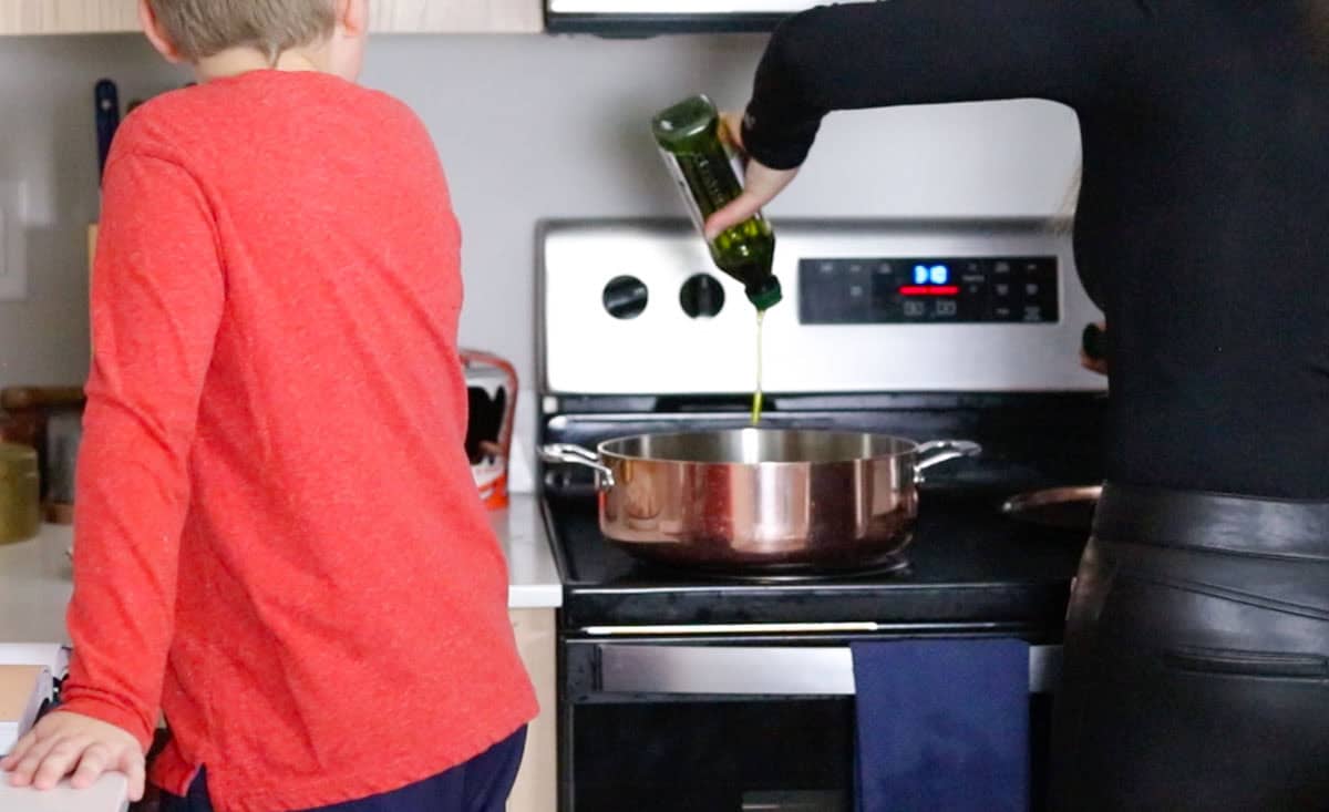 Kristin is adding oil to a rondeau at the stove