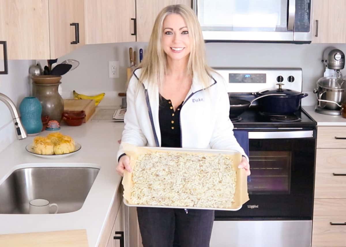 Kristin is holding a sheet pan with uncooked hash browns