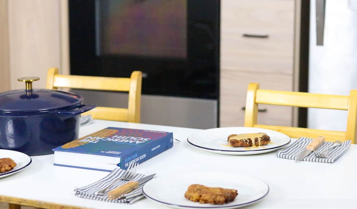 plated chicken-fried steak with pan gravy at the table beside Recipes from the American South