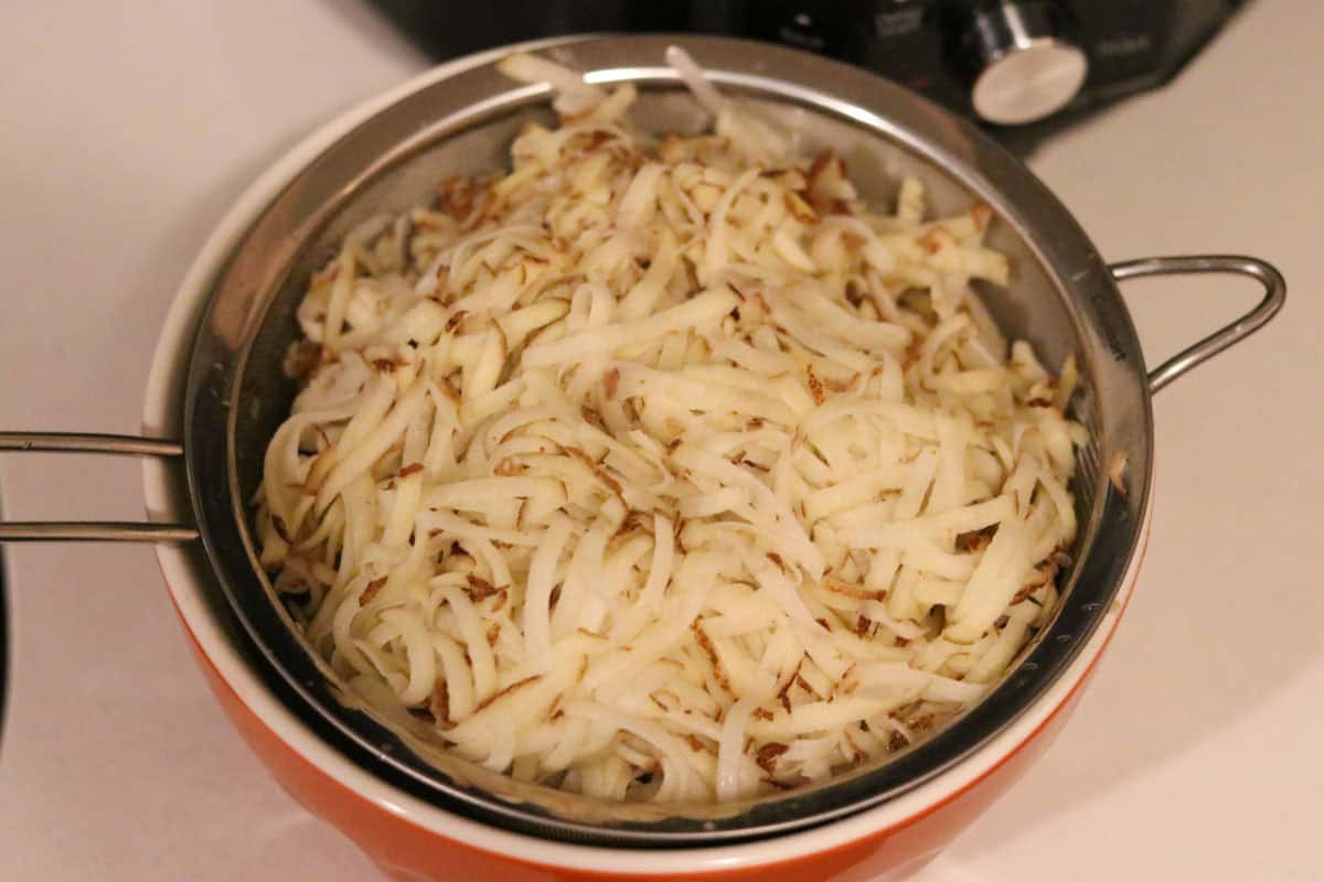 shredded potatoes in a fine mesh strainer over a bowl