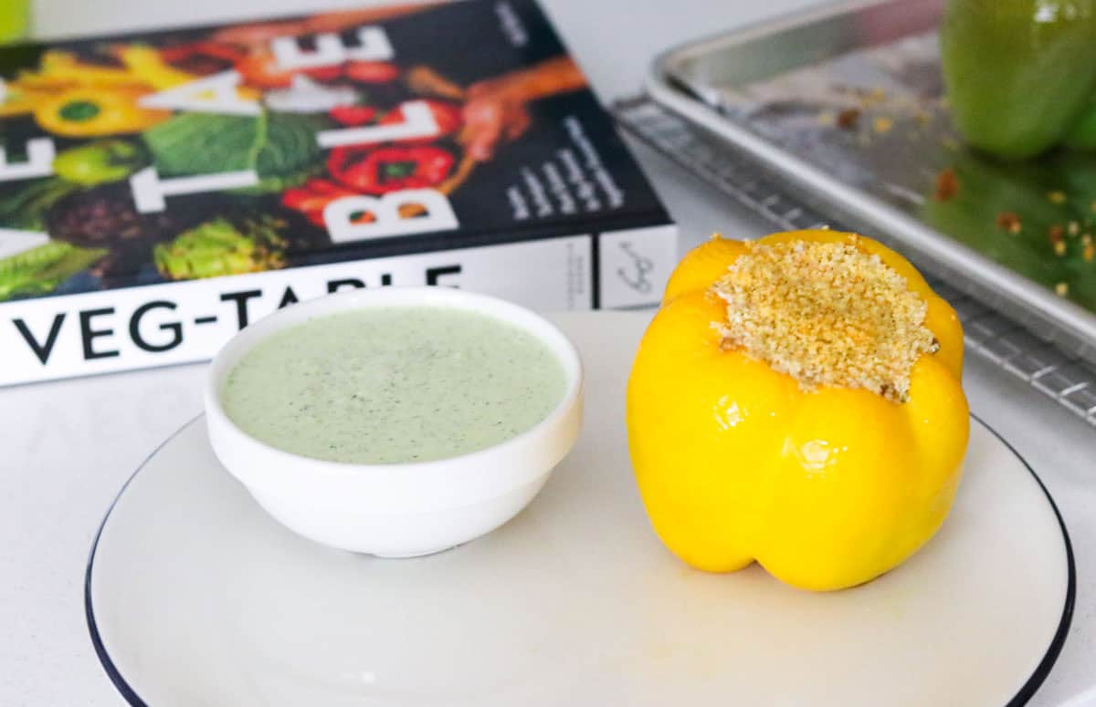 vegetarian stuffed bell pepper on a plate beside a yogurt sauce