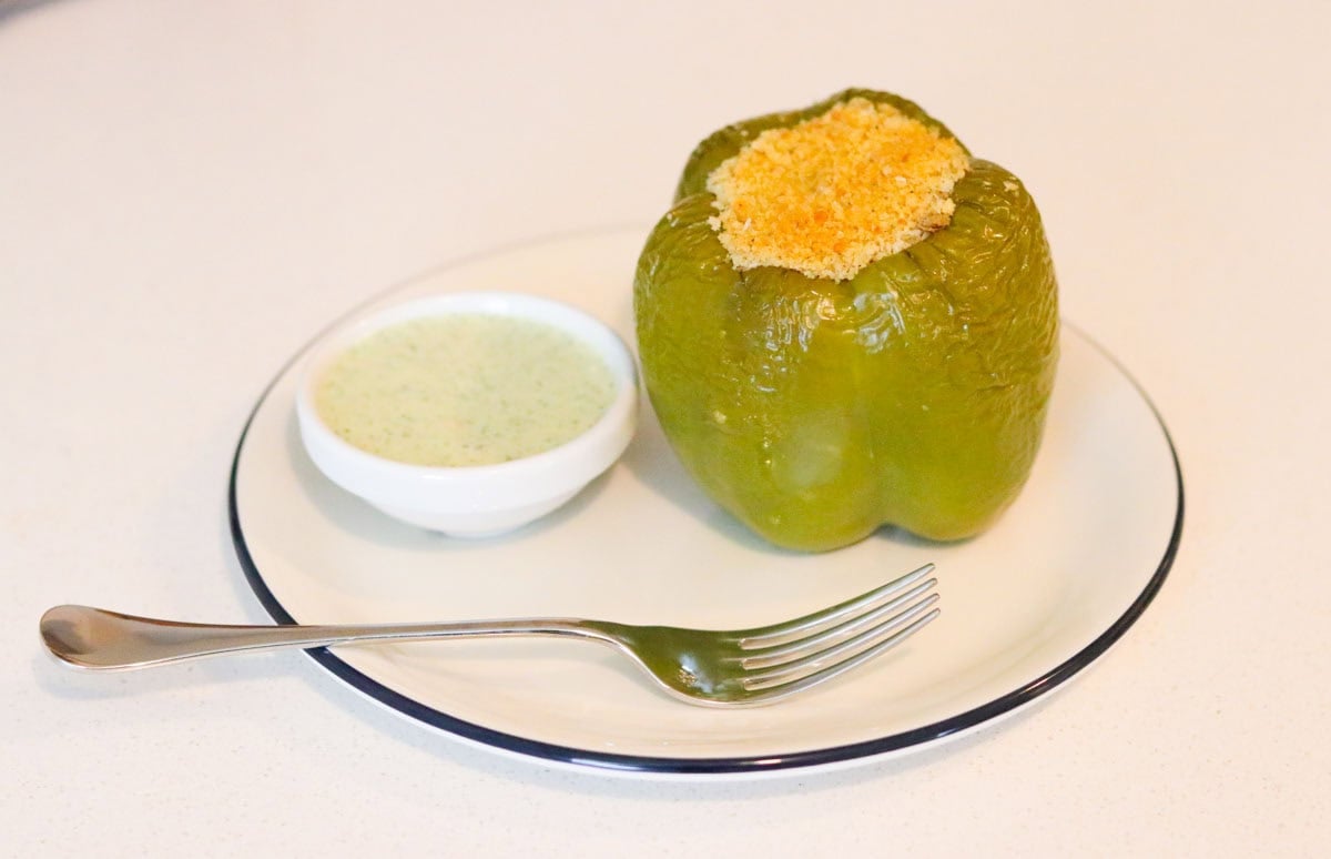 stuffed green bell pepper on a plate with a bowl of yogurt sauce