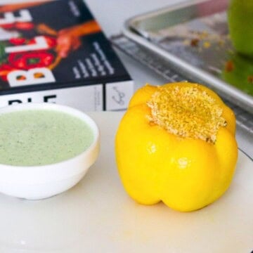 vegetarian stuffed bell pepper on a plate beside a yogurt sauce